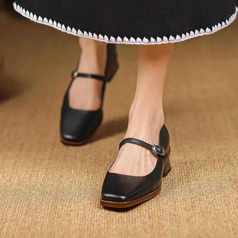 Black leather Mary Jane shoes with buckle strap worn beneath a pleated skirt