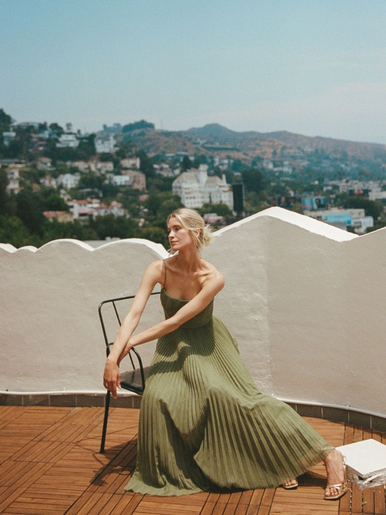 Woman seated on rooftop wearing sage pleated maxi dress with pleated skirt
