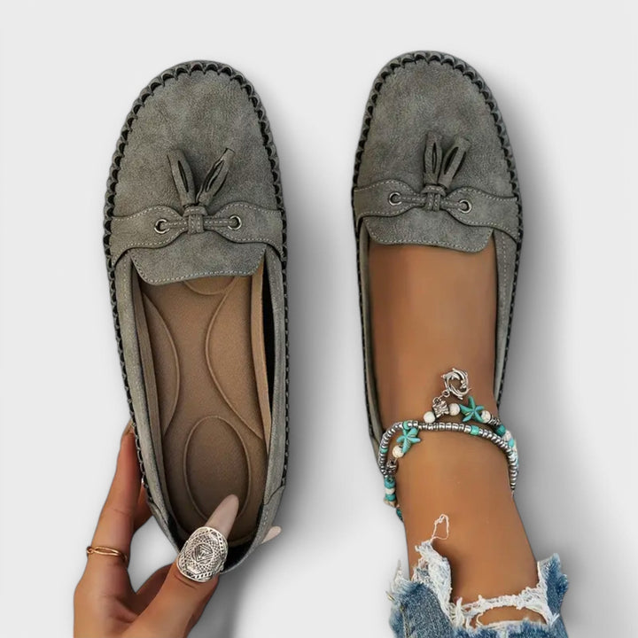 Grey suede tassel loafers viewed from above, one shoe held to show padded insole