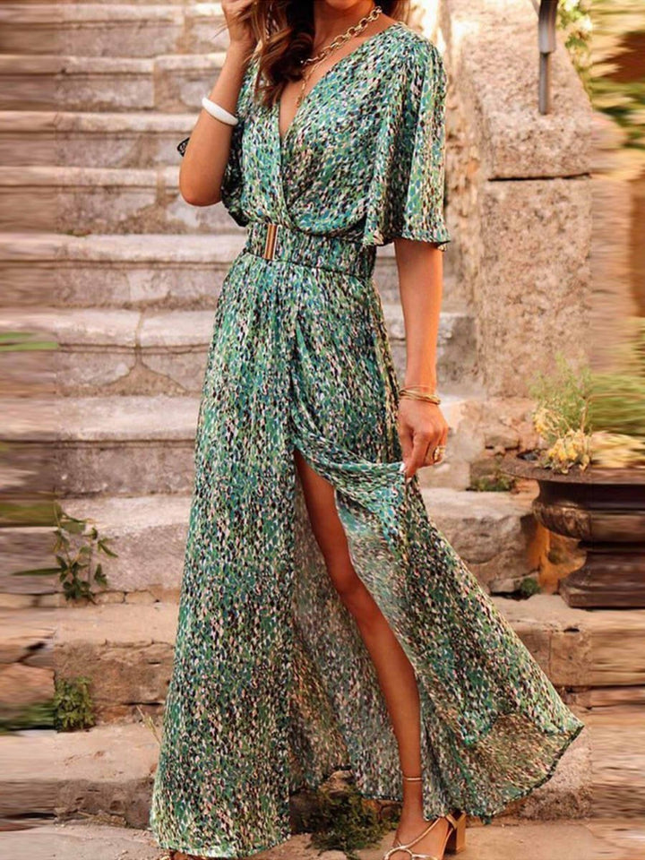 Green printed wrap maxi dress with flutter sleeves and thigh-high slit, worn on stone steps
