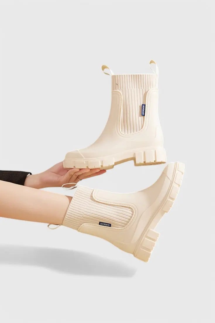 Cream waterproof Chelsea boots held by hand, displaying ribbed ankle cuff
