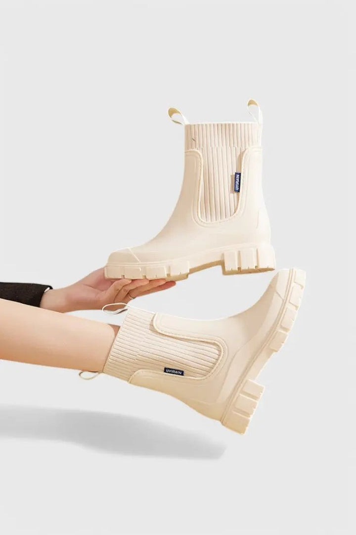 Cream waterproof Chelsea boots held by hand, displaying ribbed ankle cuff