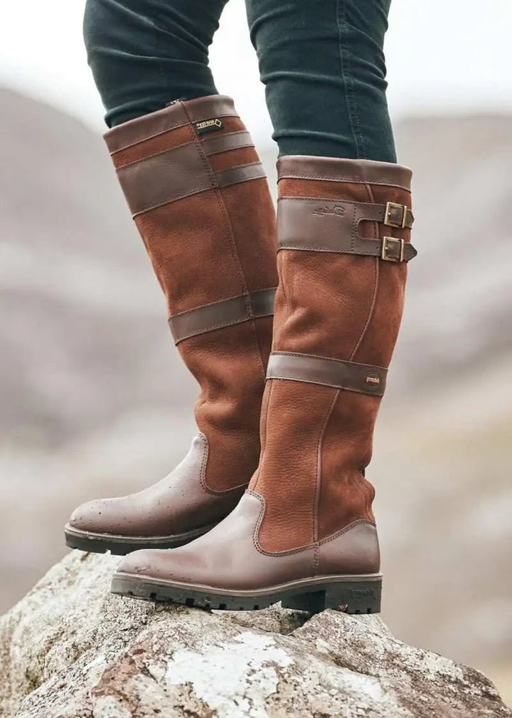 Tan knee-high waterproof leather boots with contrasting brown buckle straps, worn outdoors