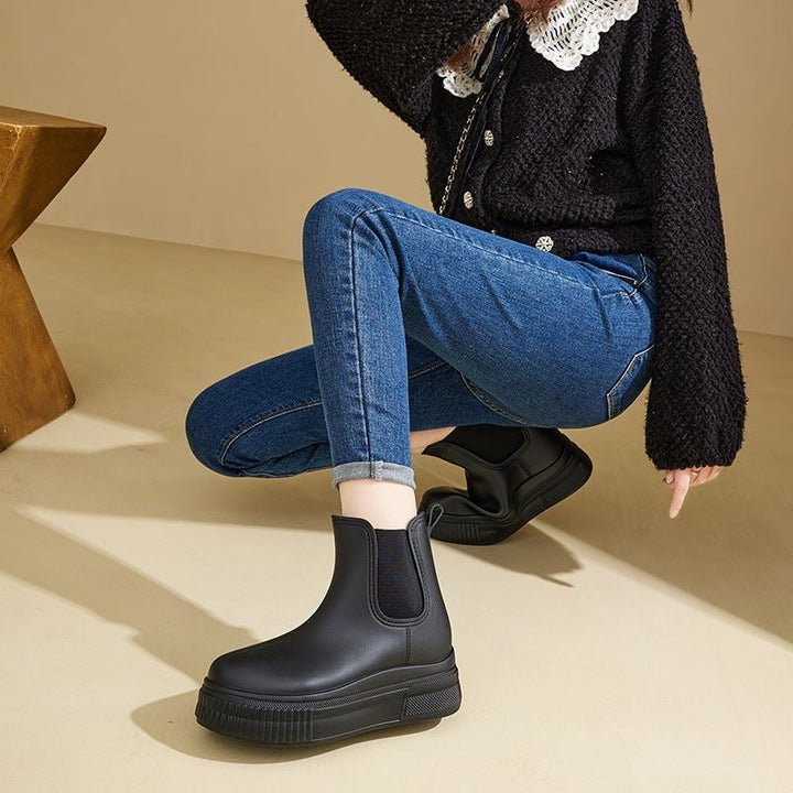 Model crouching in black Chelsea platform rain boots with cuffed jeans