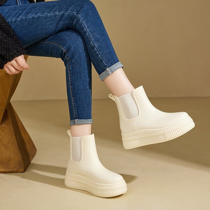 Model in cuffed jeans wearing cream platform Chelsea rain boots seated