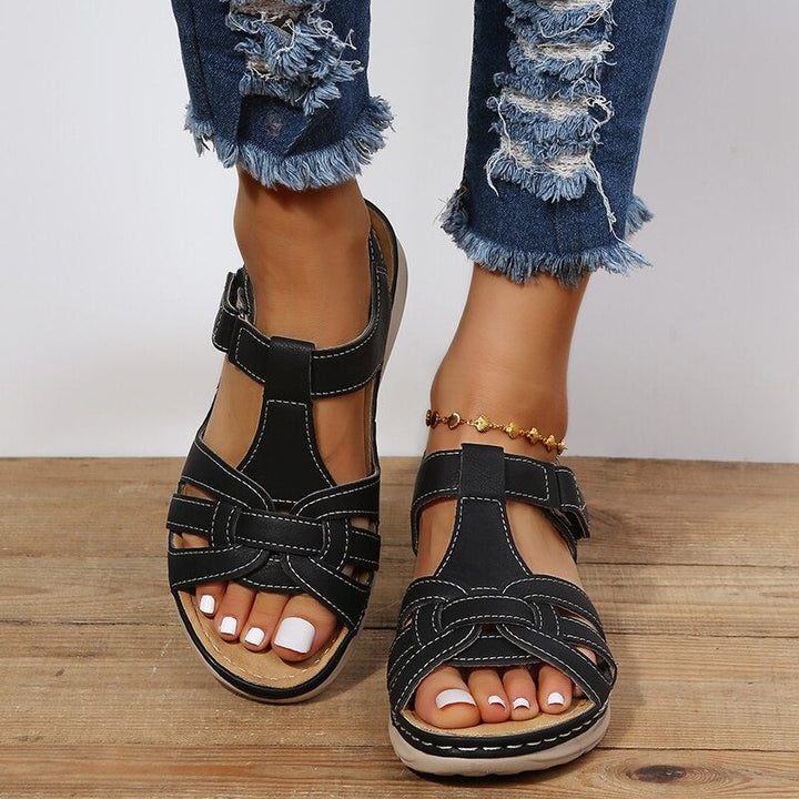 black T-bar wedge sandals worn on feet with cushioned tan footbed