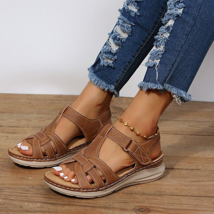 tan woven T-bar sandals with buckle strap worn on wooden decking